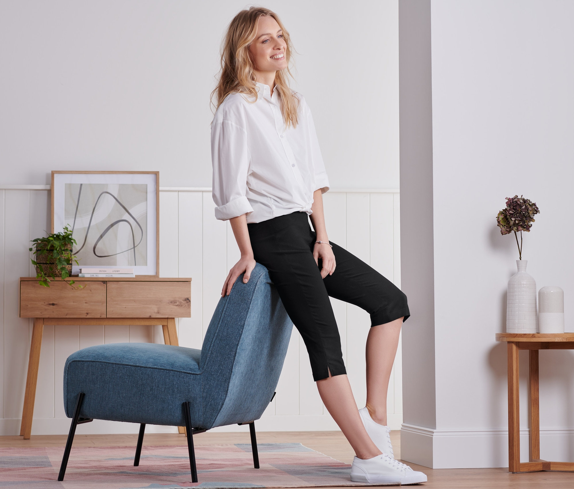 Kobieta siedzi na niebieskim krześle i ma na sobie czarne spodnie z bengaliny o długości 3/4.