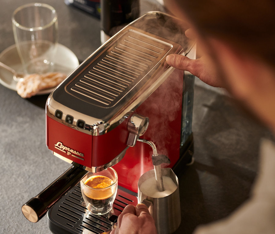 Mężczyzna przygotowuje kawę i spienia mleko za pomocą czerwonego ekspresu kolbowego do kawy »Lapressa«.