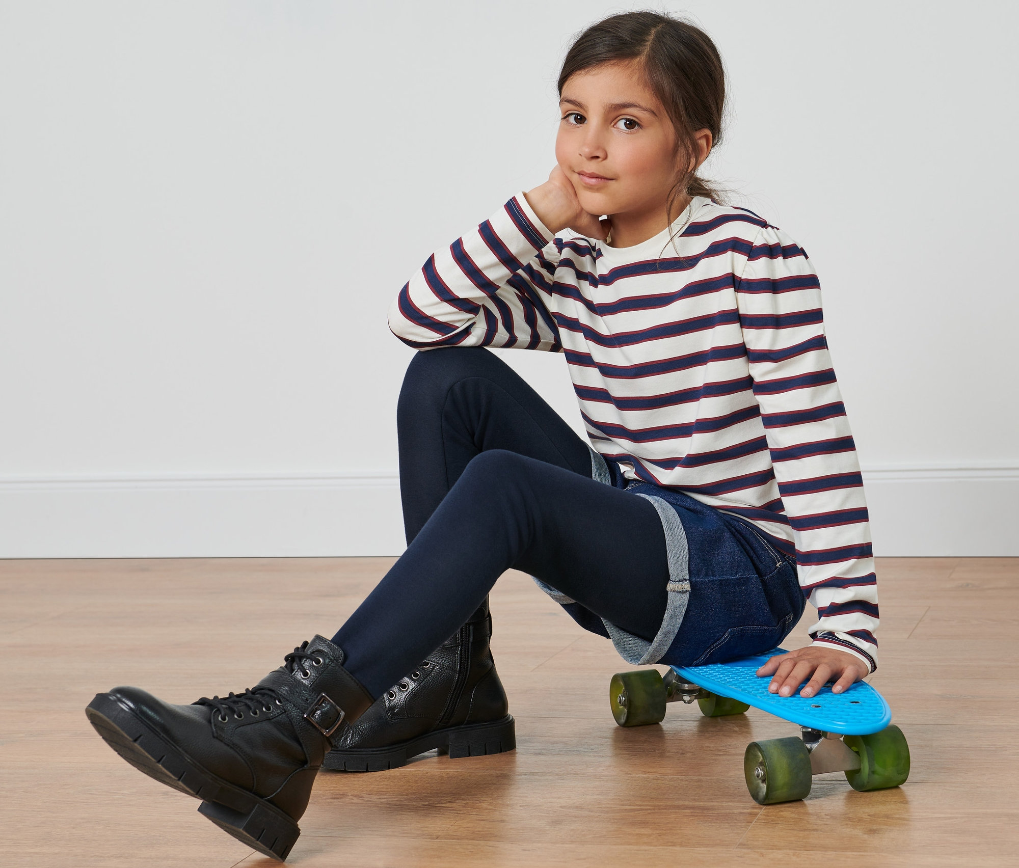 Dziewczyna siedzi na deskorolce w dziecięcych legginsach termicznych i koszulce w paski.