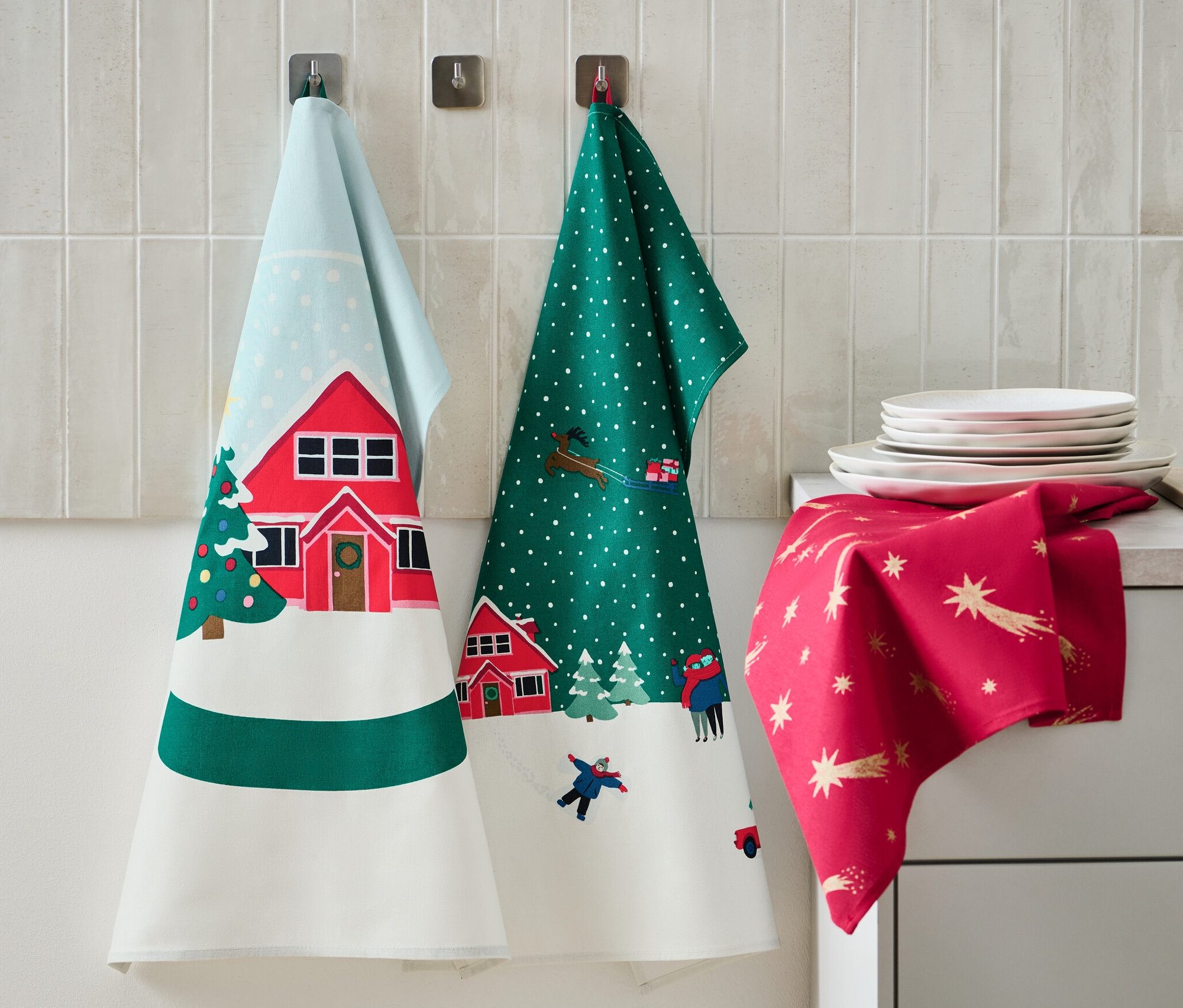 Na ścianie wiszą 3 ściereczki do naczyń z motywami świątecznymi. Na blacie leżą talerze i dozownik mydła.