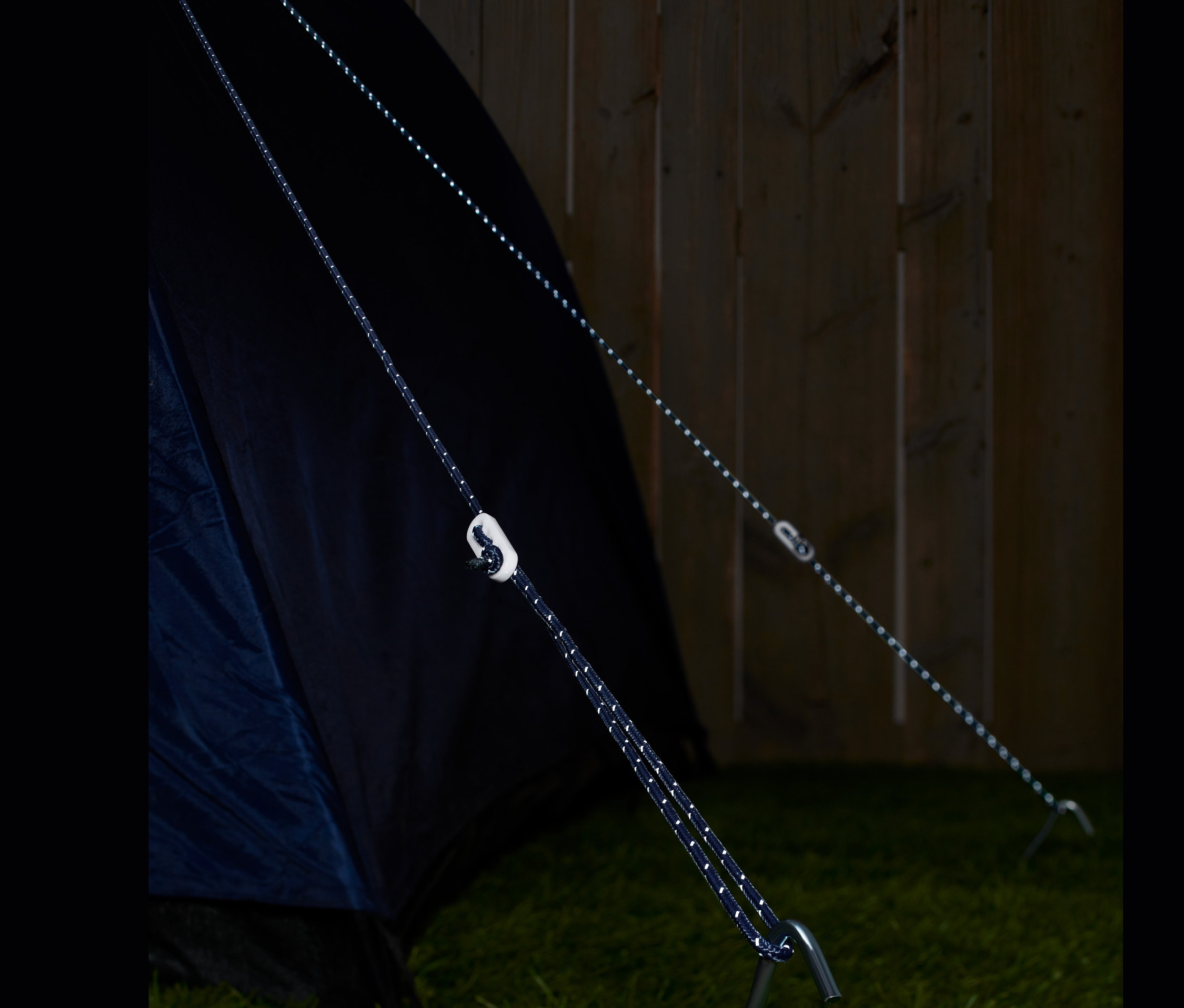 Dwa odblaskowe odciągi przymocowane są do namiotu i kołka w trawie.