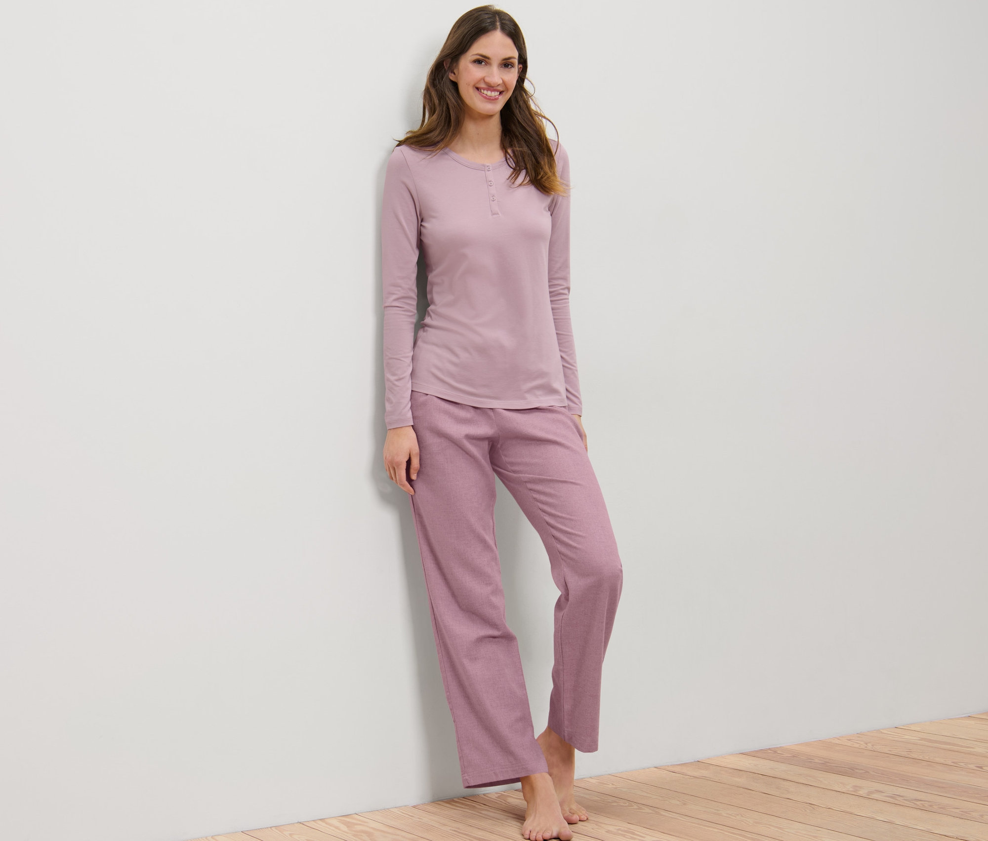 Kobieta opiera się o ścianę w piżamie flanelowej.
