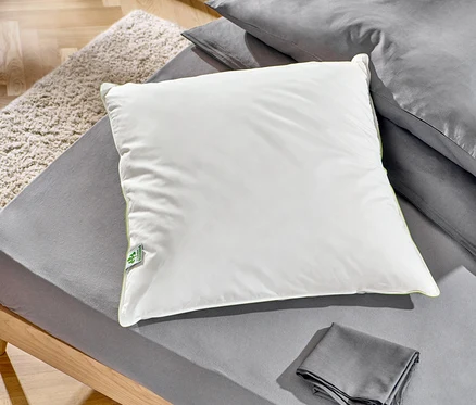 Na łóżku leżą dwie poduszki z pierza irisette® greenline: jedna ok. 90 x 70 cm, a druga ok. 80 x 80 cm.