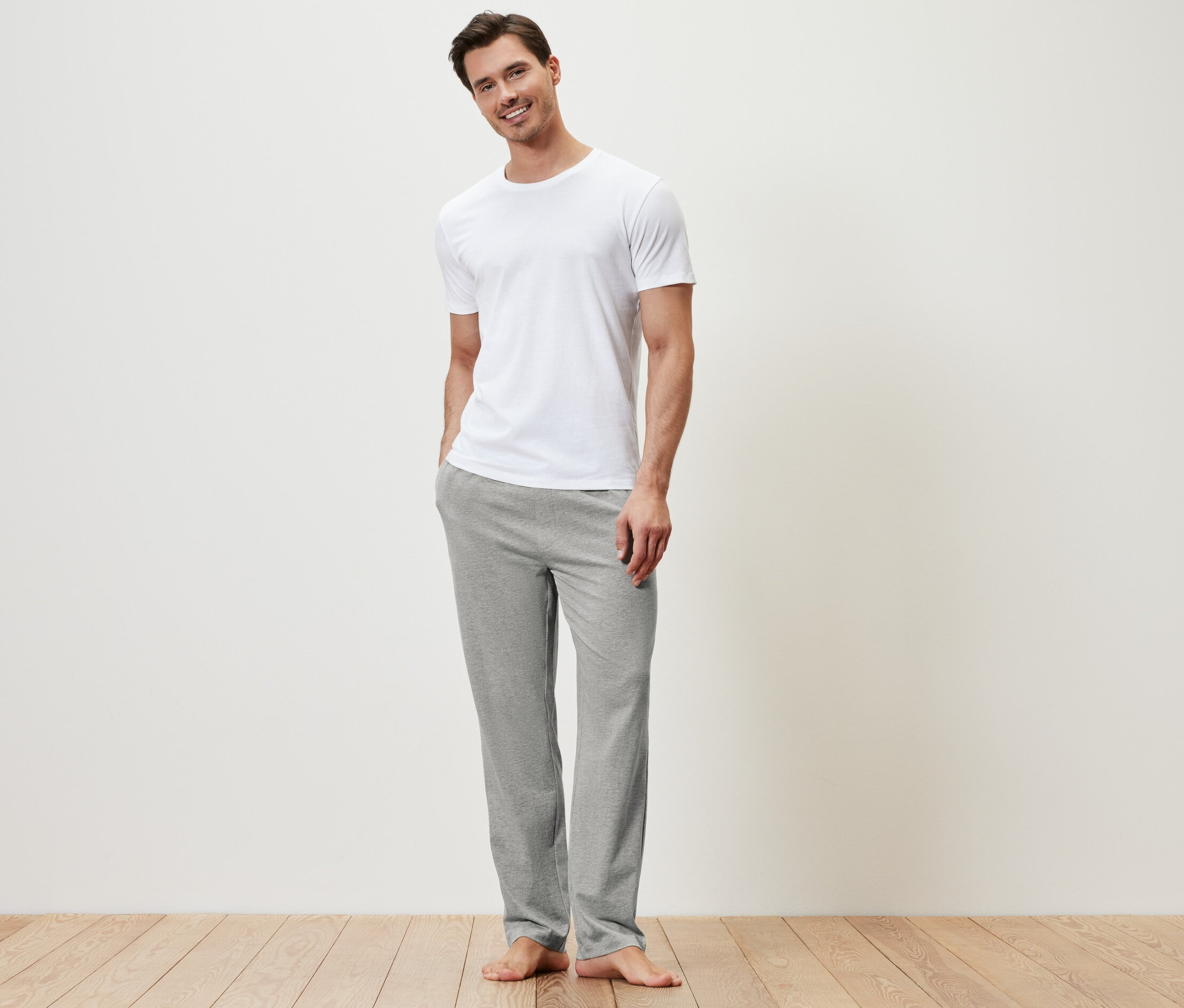 Mężczyzna stoi w białej koszulce i szarych spodniach rekreacyjnych.