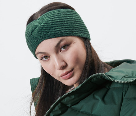 Kobieta ma na sobie ciemnozieloną opaskę z dzianiny i zieloną kurtkę.