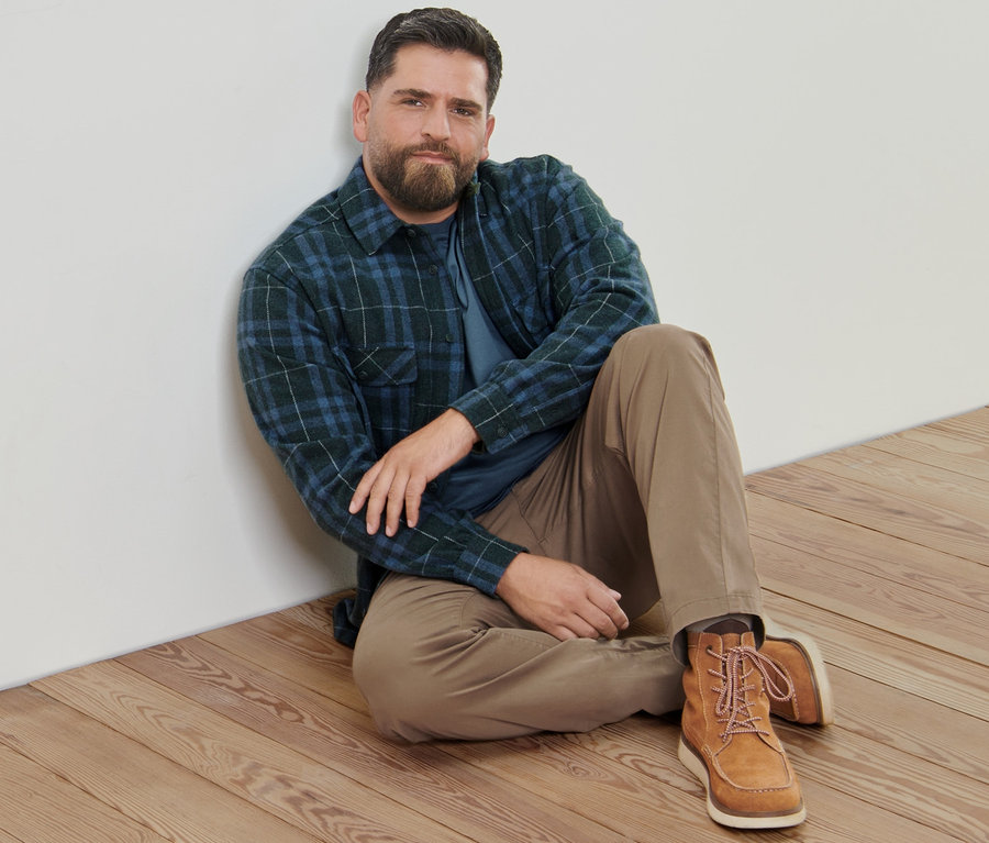 Mężczyzna siedzi na drewnianej podłodze, ubrany w piaskowe spodnie w stylu chino, flanelową kurtkę koszulową i koszulki z długim rękawem (2 sztuki).