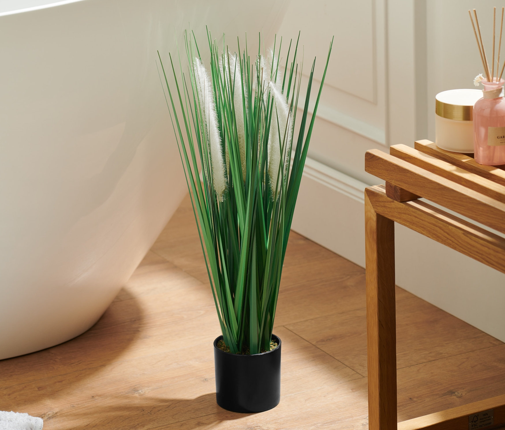 W łazience obok wanny stoi sztuczna roślina w doniczce.