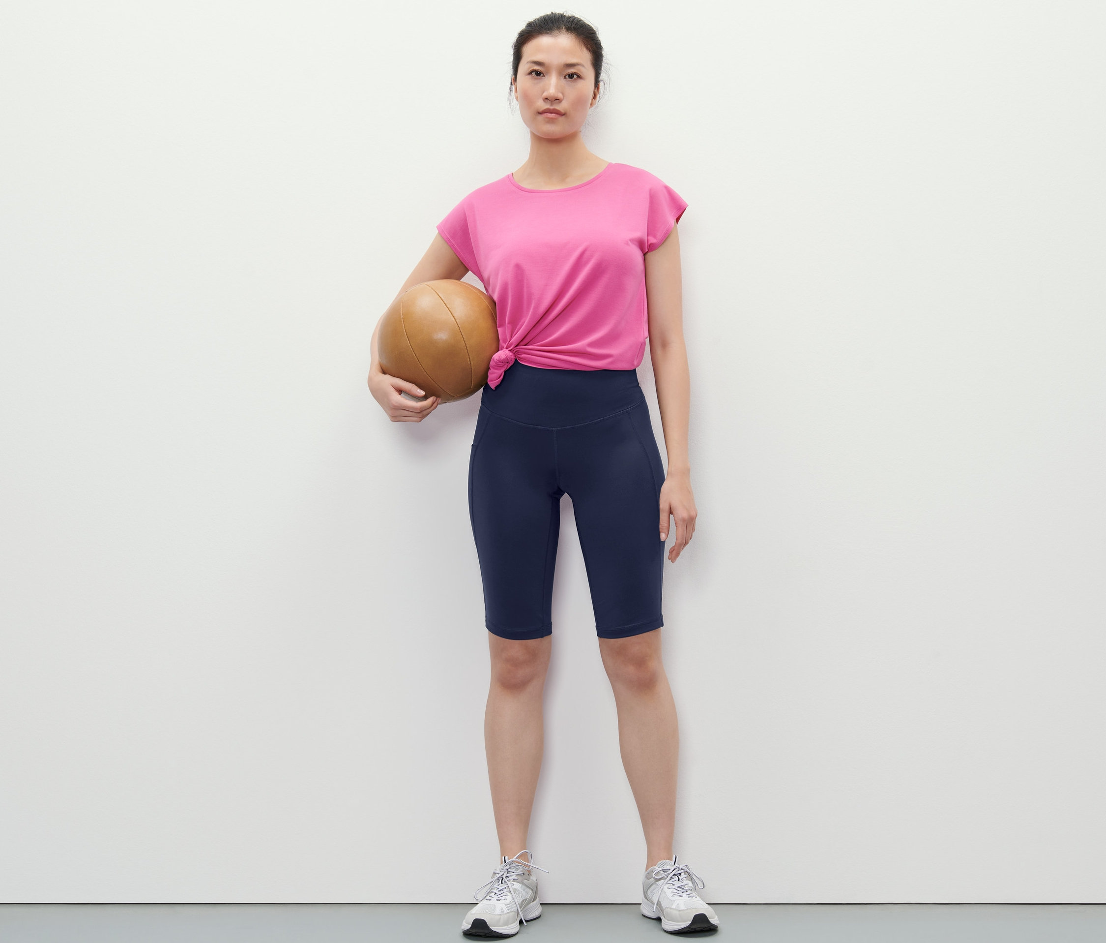 Kobieta trzyma piłkę do koszykówki i ma na sobie granatowe kolarki.