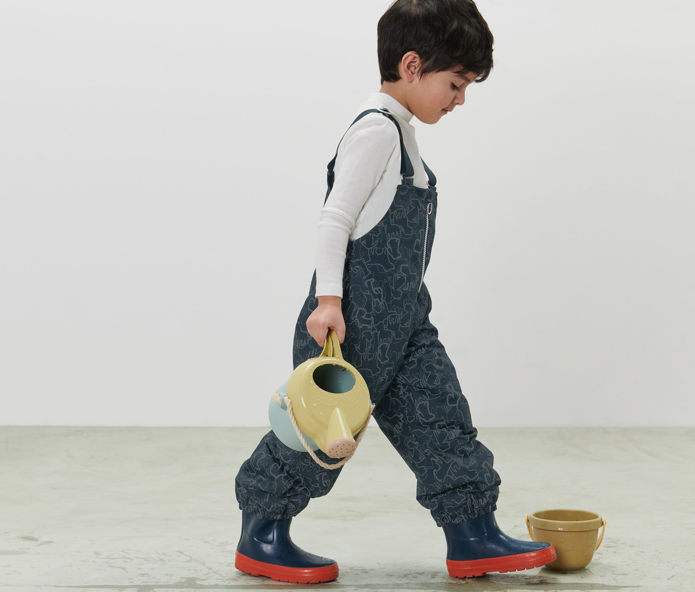 Chłopiec idzie i niesie konewkę. Ma na sobie granatowe dziecięce spodnie termoaktywne z elementami odblaskowymi.