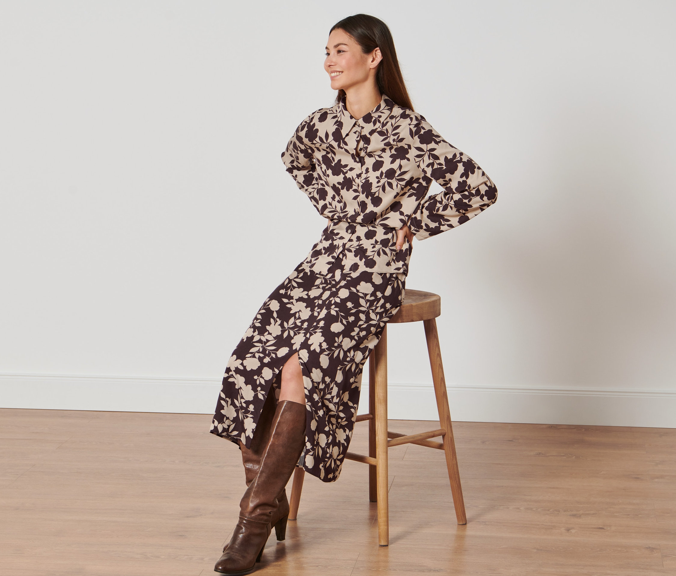 Kobieta siedzi na stołku i ma na sobie spódnicę z nadrukiem na całej powierzchni.