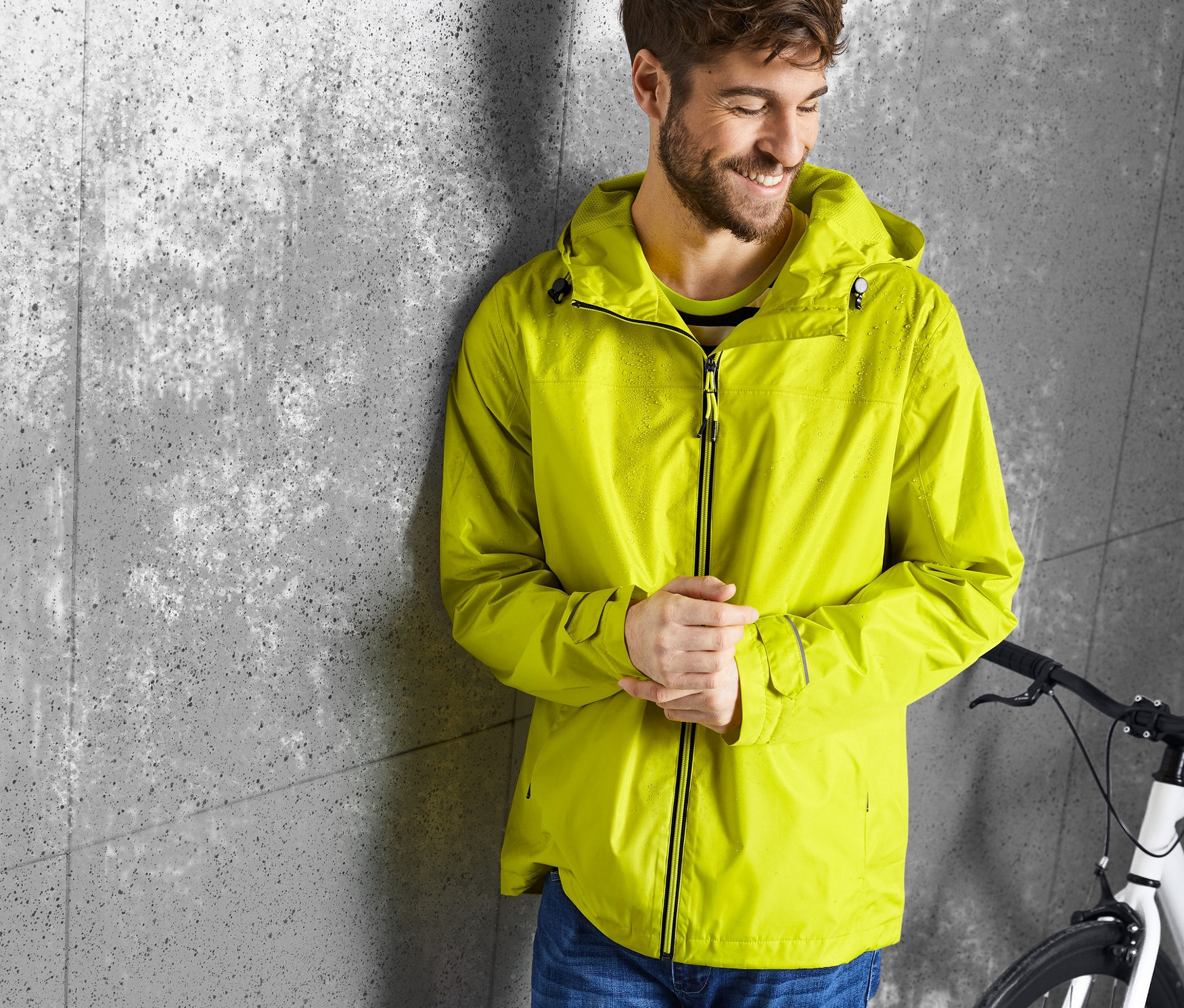 Mężczyzna oparty o ścianę ma na sobie żółtą kurtkę przeciwdeszczową.