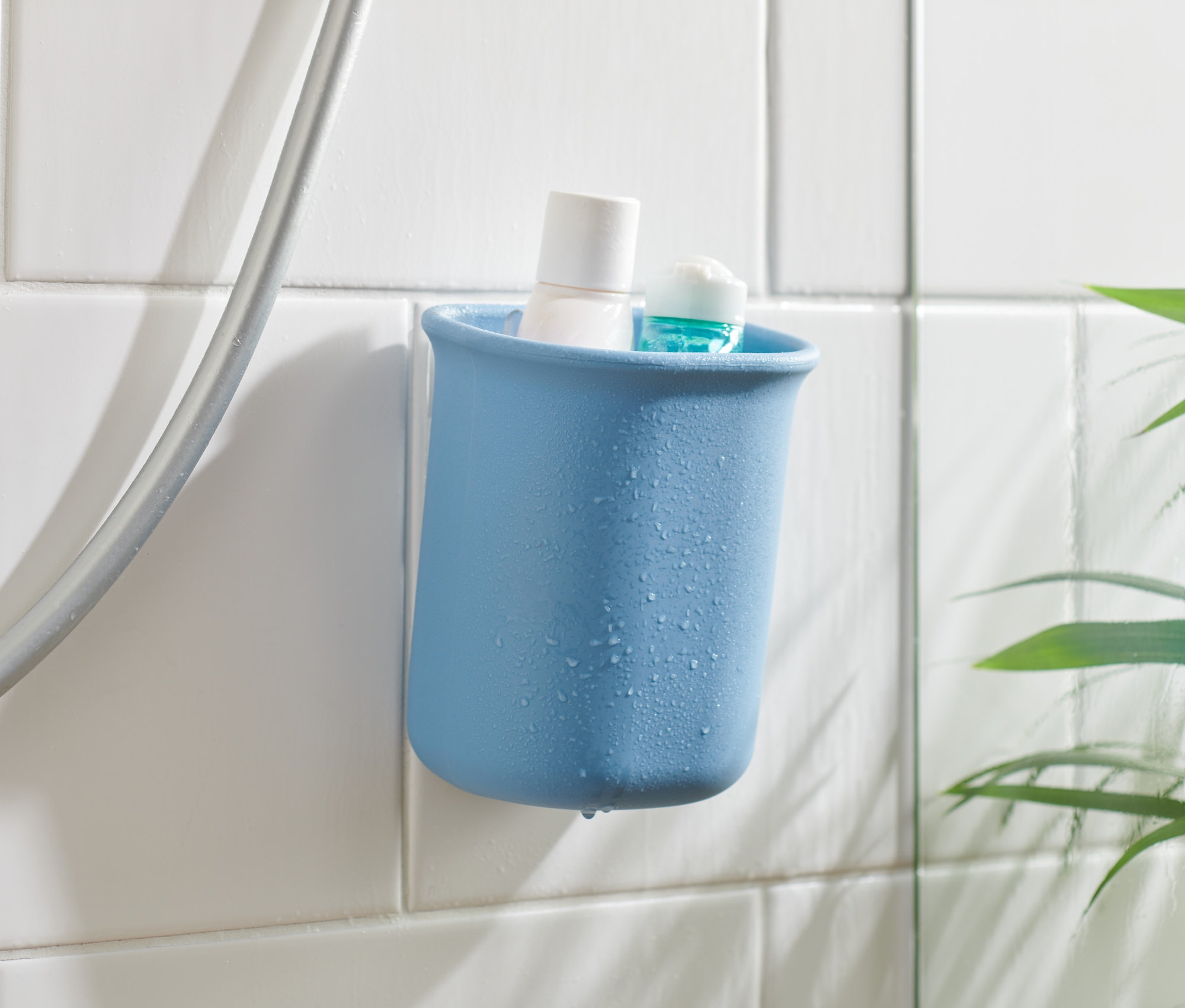 Niebieski organizer do łazienki z białym i niebieskim produktem w środku, przymocowany do białych płytek obok węża prysznicowego.