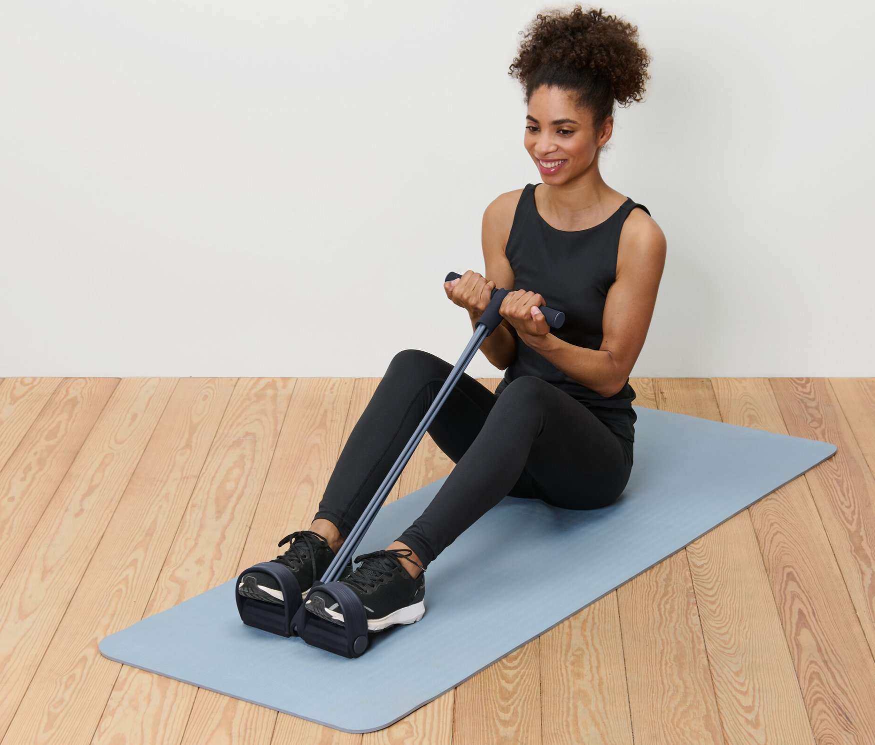 Kobieta siedzi na macie i używa przyrządu do treningu mięśni brzucha i pleców.