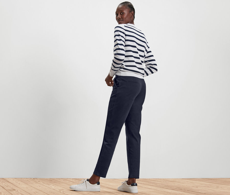 Kobieta pozuje w granatowych spodniach chinosach i pasiastym swetrze.