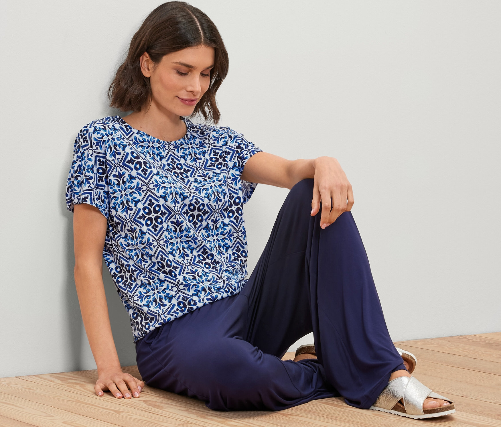 Kobieta siedzi na podłodze, ubrana w niebieską bluzkę z nadrukiem.