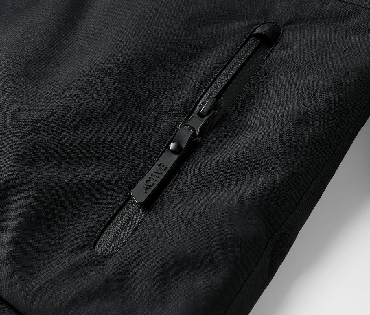 Szczegół czarnego zamka błyskawicznego w kurtce z napisem ACTIVE.