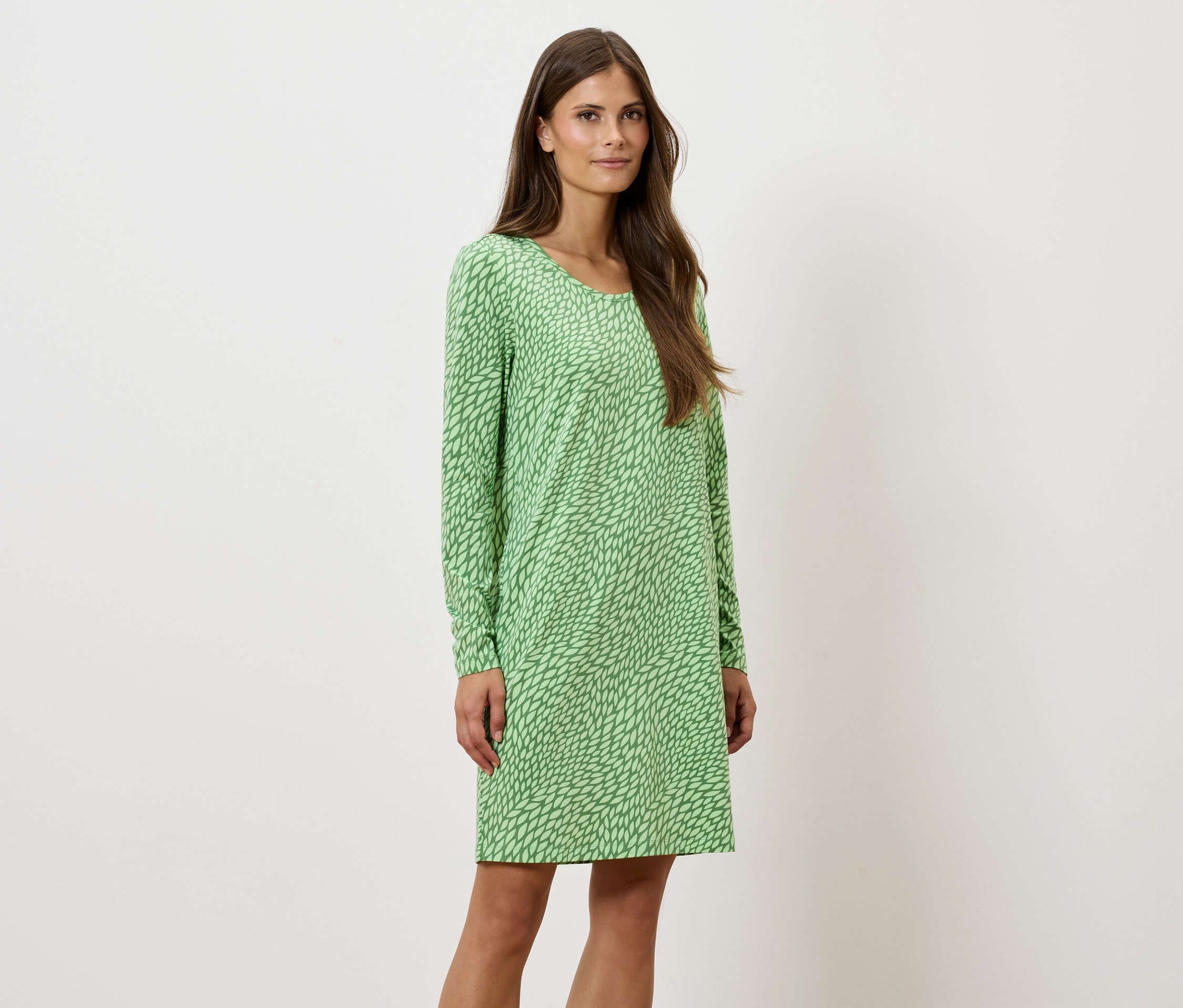 Kobieta stoi i pozuje w zielonej wzorzystej sukience z długim rękawem.