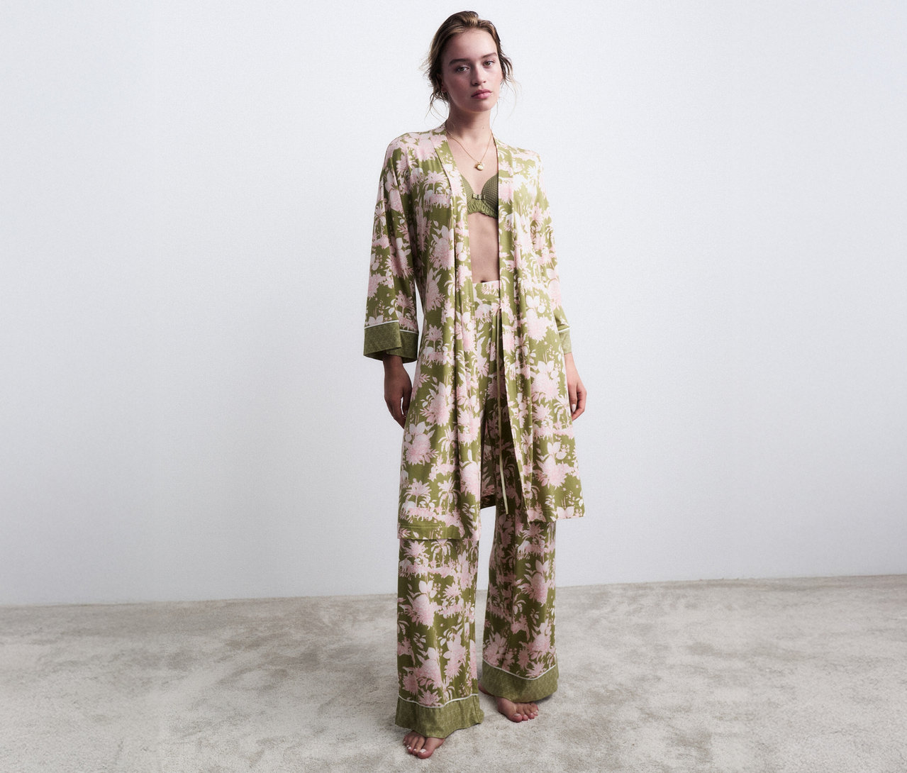 Kobieta stoi boso w zielonej piżamie w kwiaty z pasującym szlafrokiem.