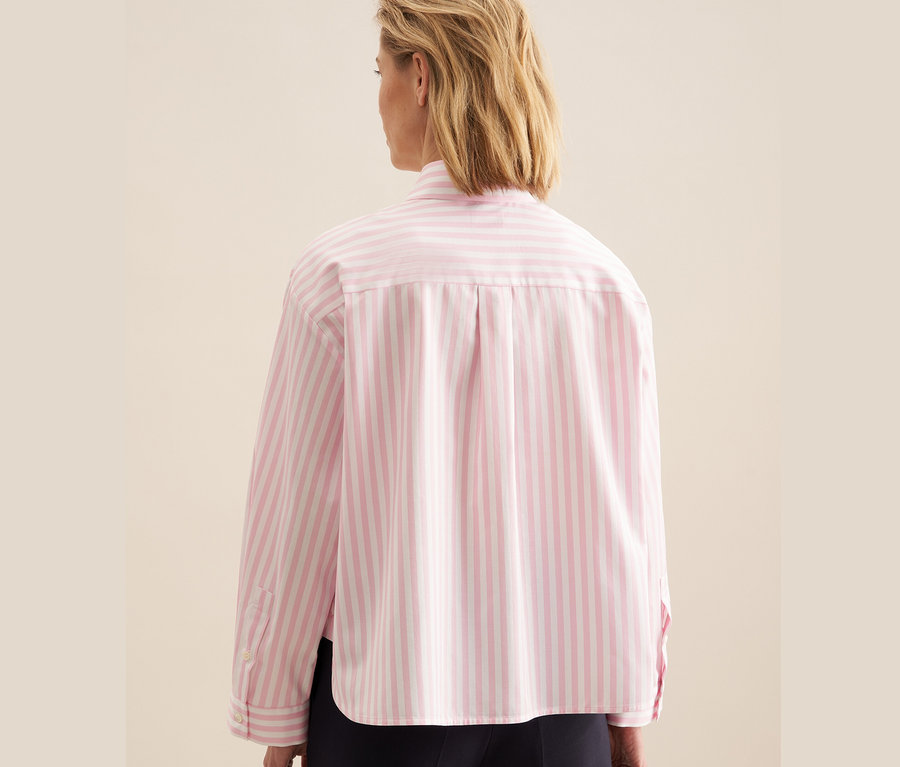 Kobieta ma na sobie różową bluzkę koszulową oversize w białe paski marki Seidensticker.