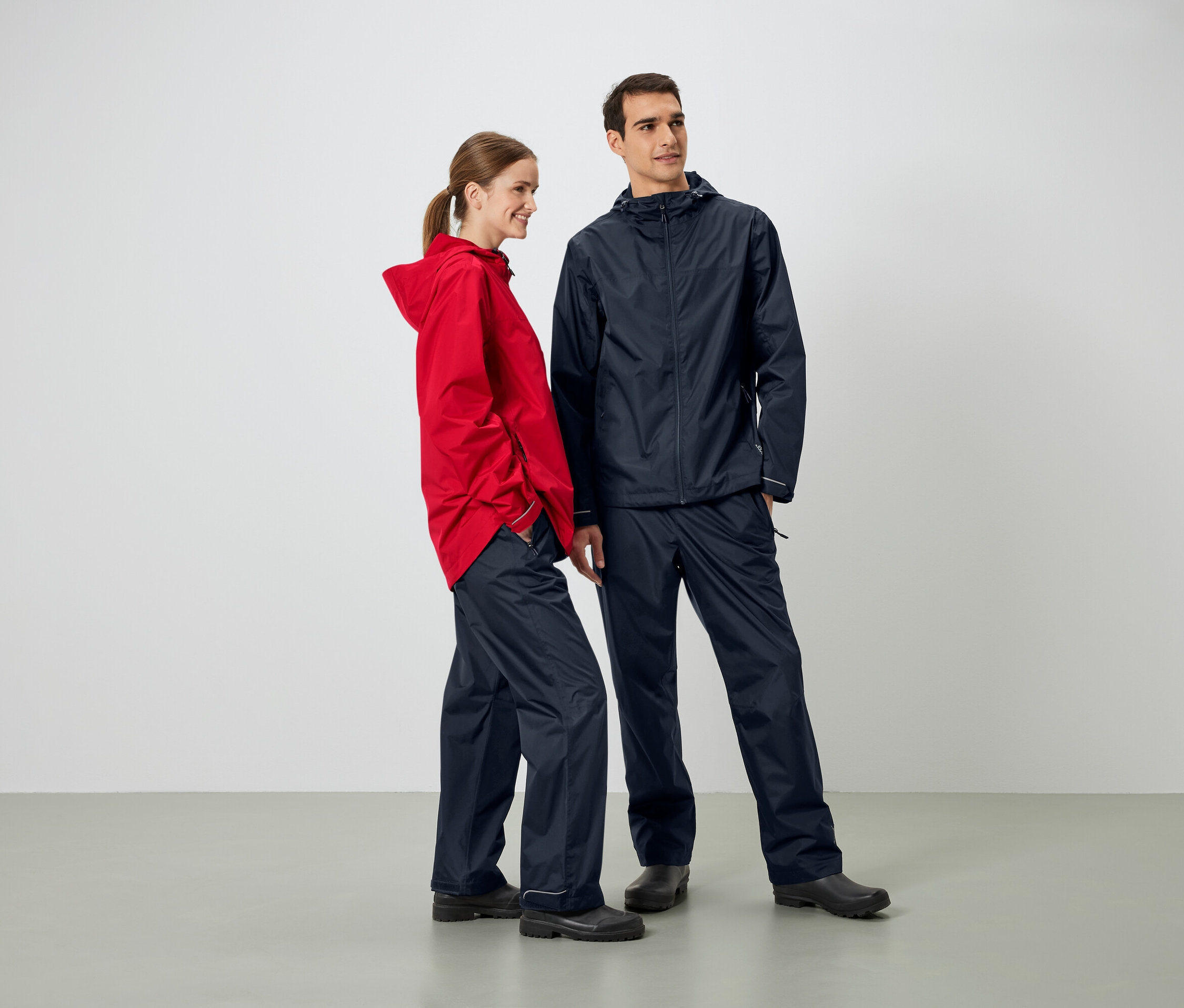 Mężczyzna i kobieta stoją obok siebie w kurtkach i spodniach przeciwdeszczowych.