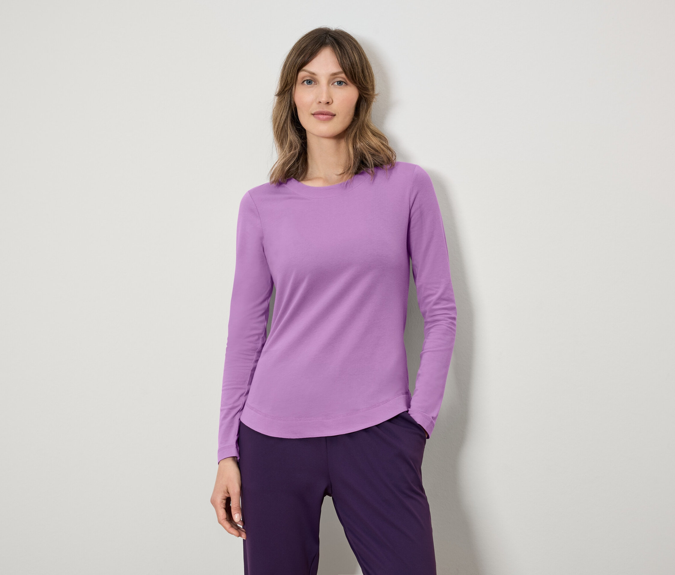 Kobieta ma na sobie fioletową koszulkę z długim rękawem i ciemnofioletowe spodnie.
