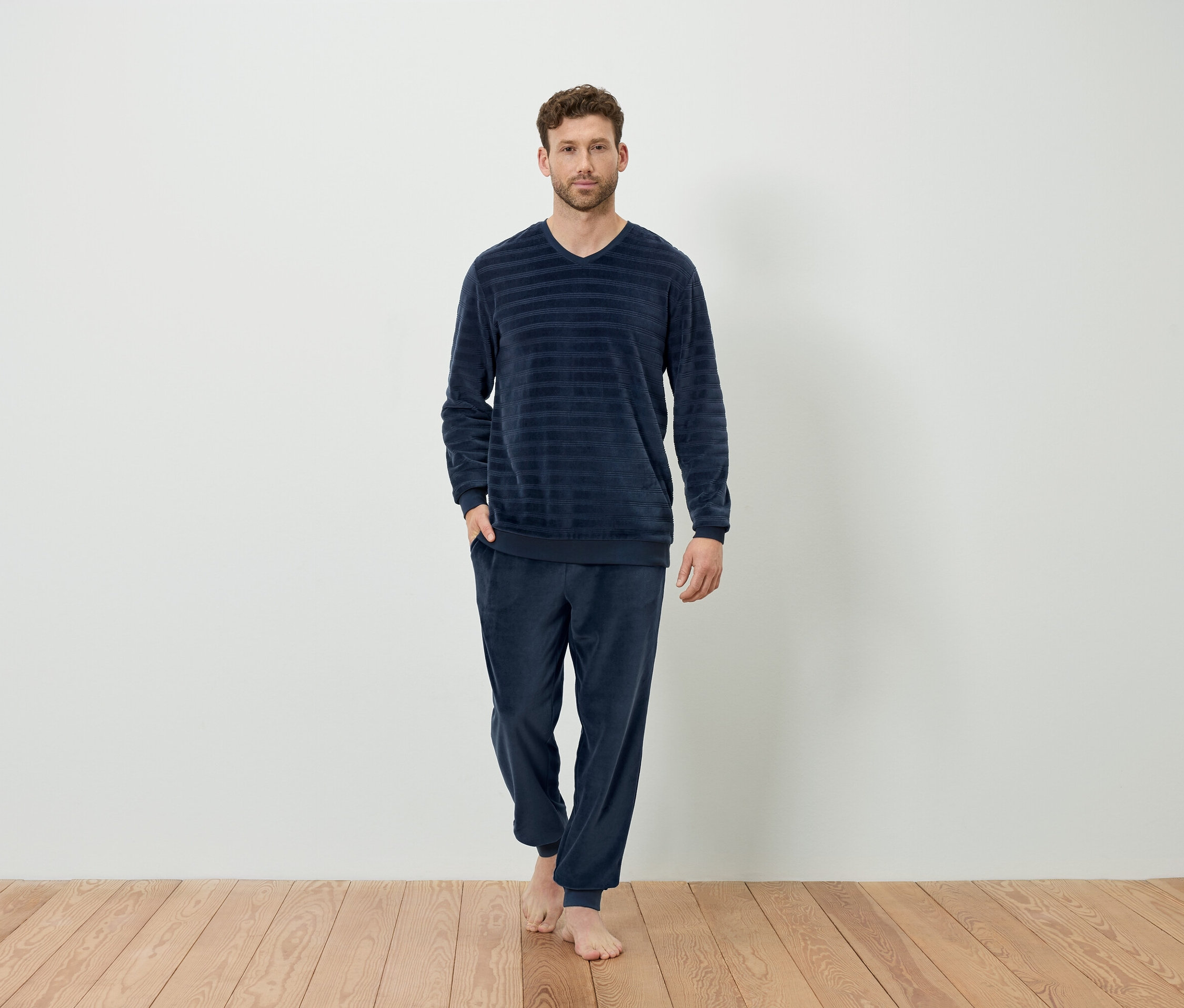Mężczyzna stoi boso ubrany w granatową piżamę w paski.