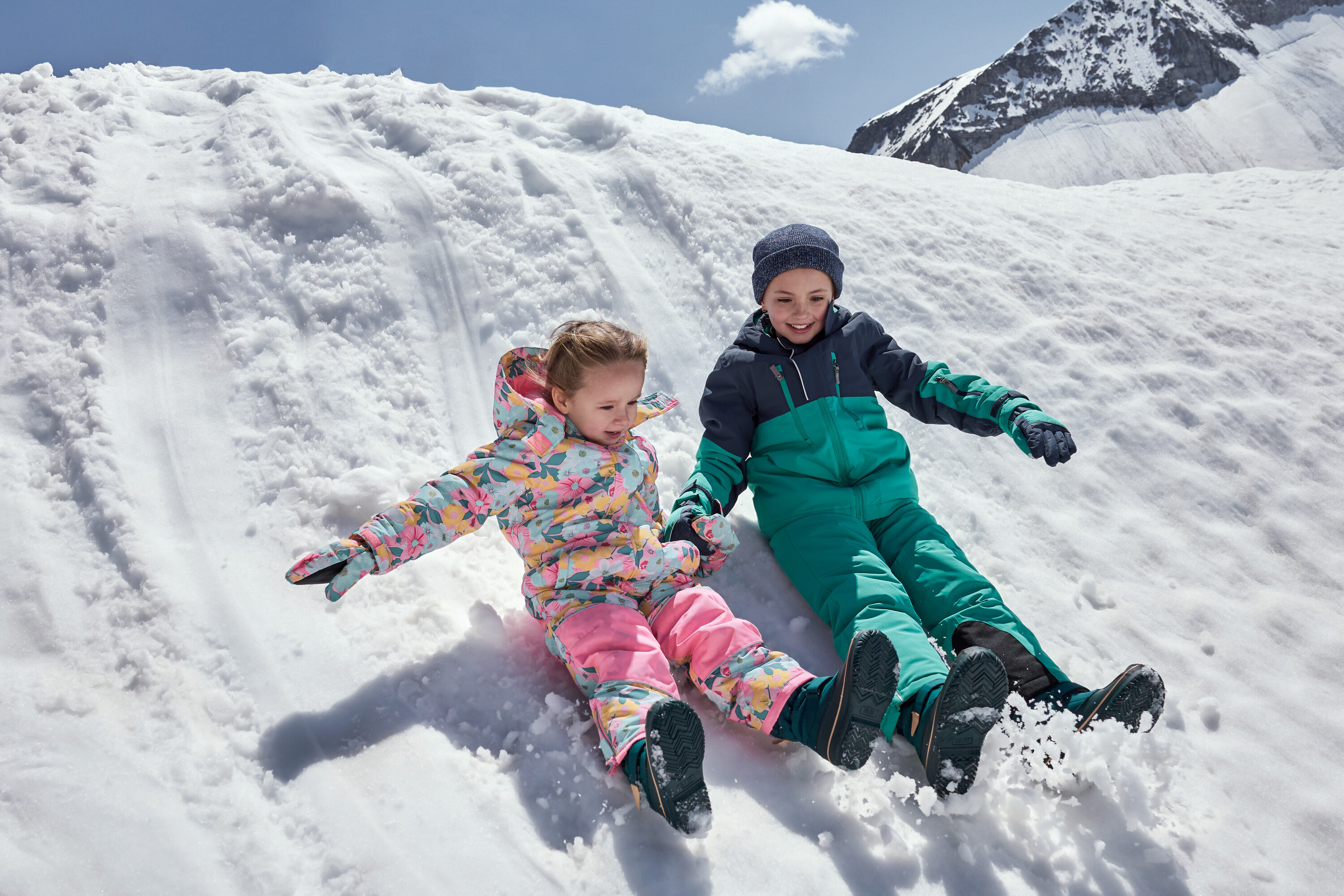 Dzieci zjeżdżają ze śnieżnego wzgórza w kolorowych kombinezonach zimowych.