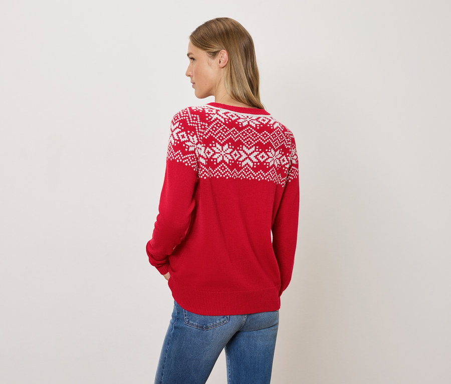 Kobieta patrzy przez ramię, ubrana w czerwony sweter w norweskie wzory i dżinsy.