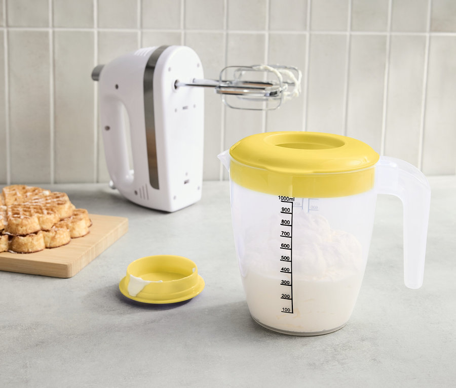 Na blacie stoi biały mikser, miarka z żółtą pokrywką wypełniona płynem i stos wafli na desce.