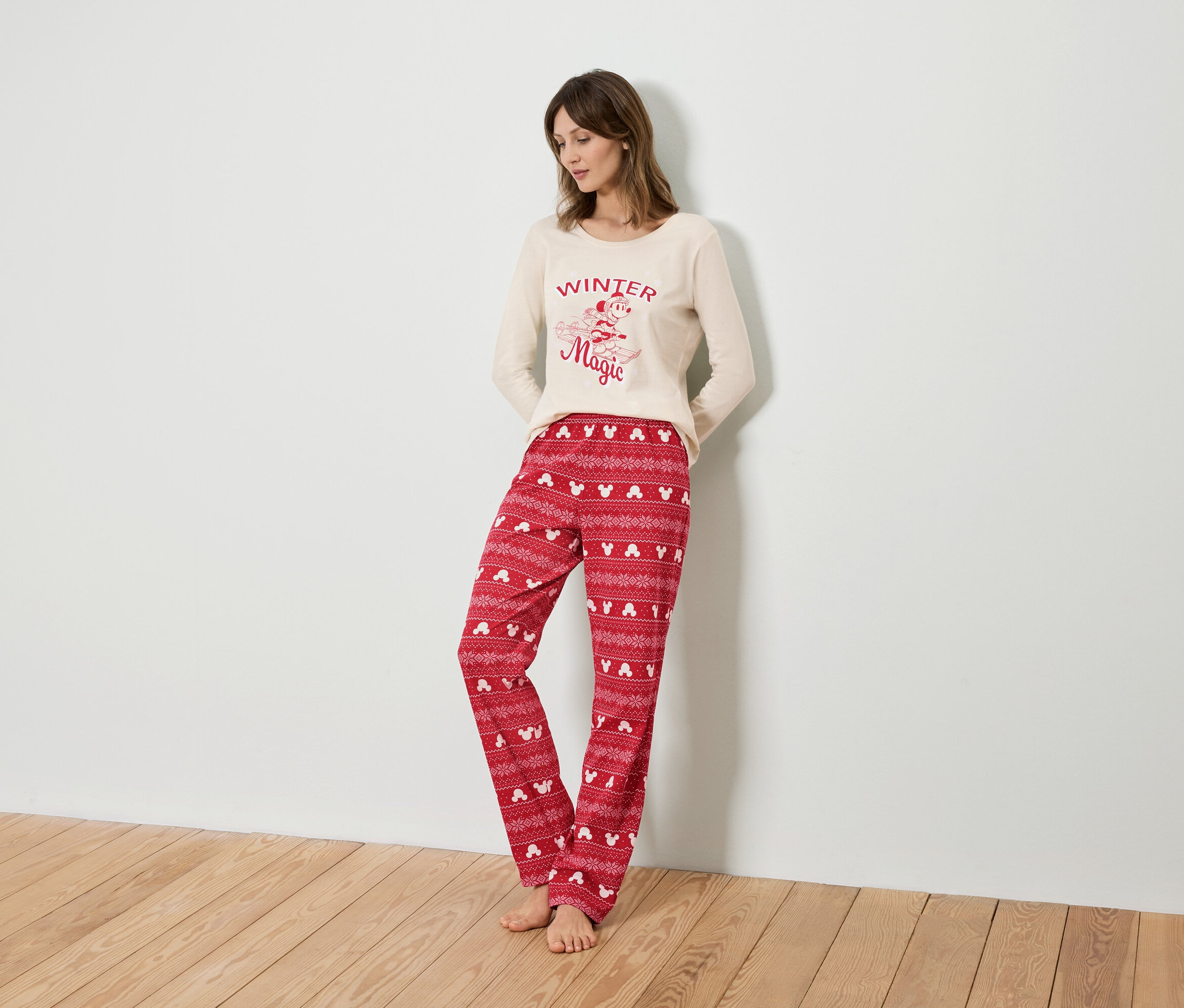 Kobieta ubrana w beżową bluzkę od piżamy z długim rękawem i czerwone spodnie od piżamy z motywem Myszki Miki.