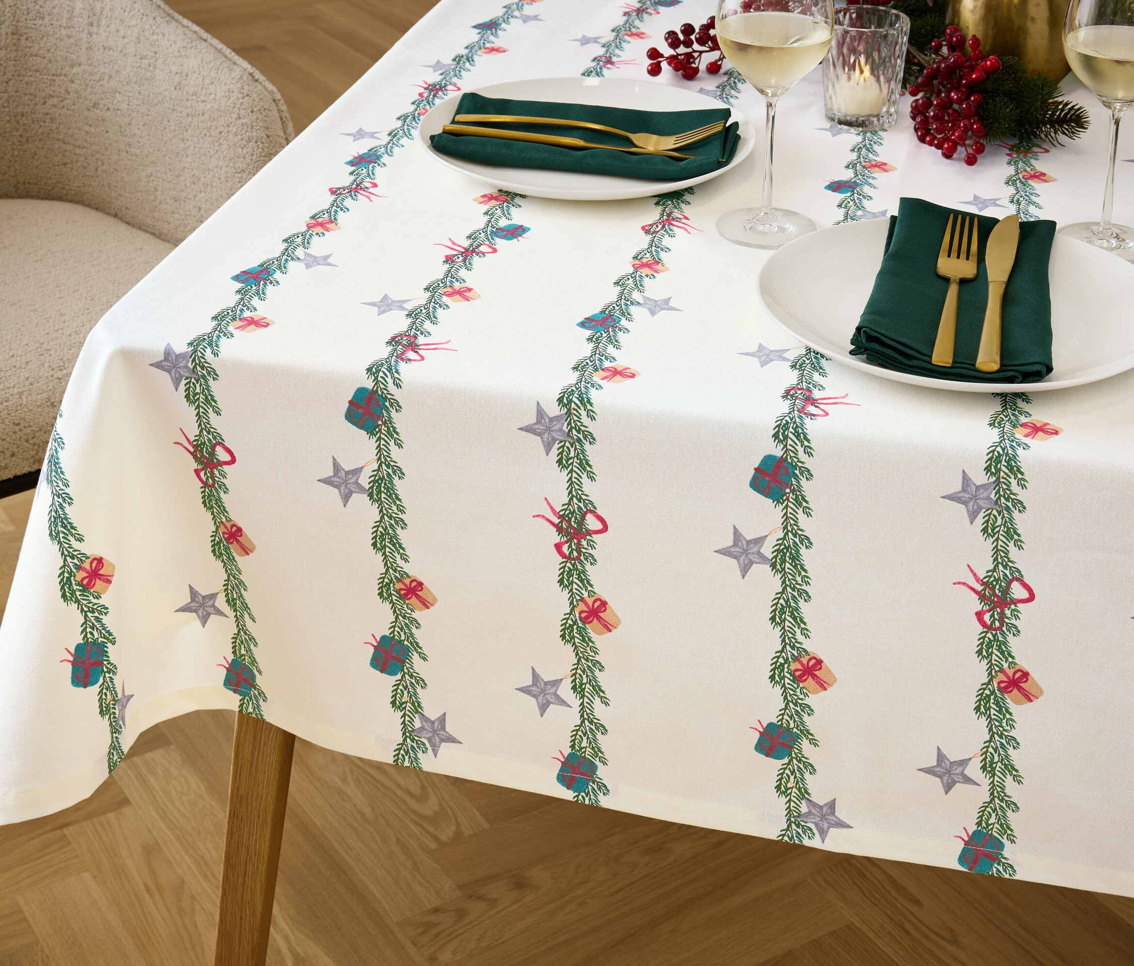 Szczegół stołu z świątecznym obrusem, talerzami, sztućcami i szklankami.