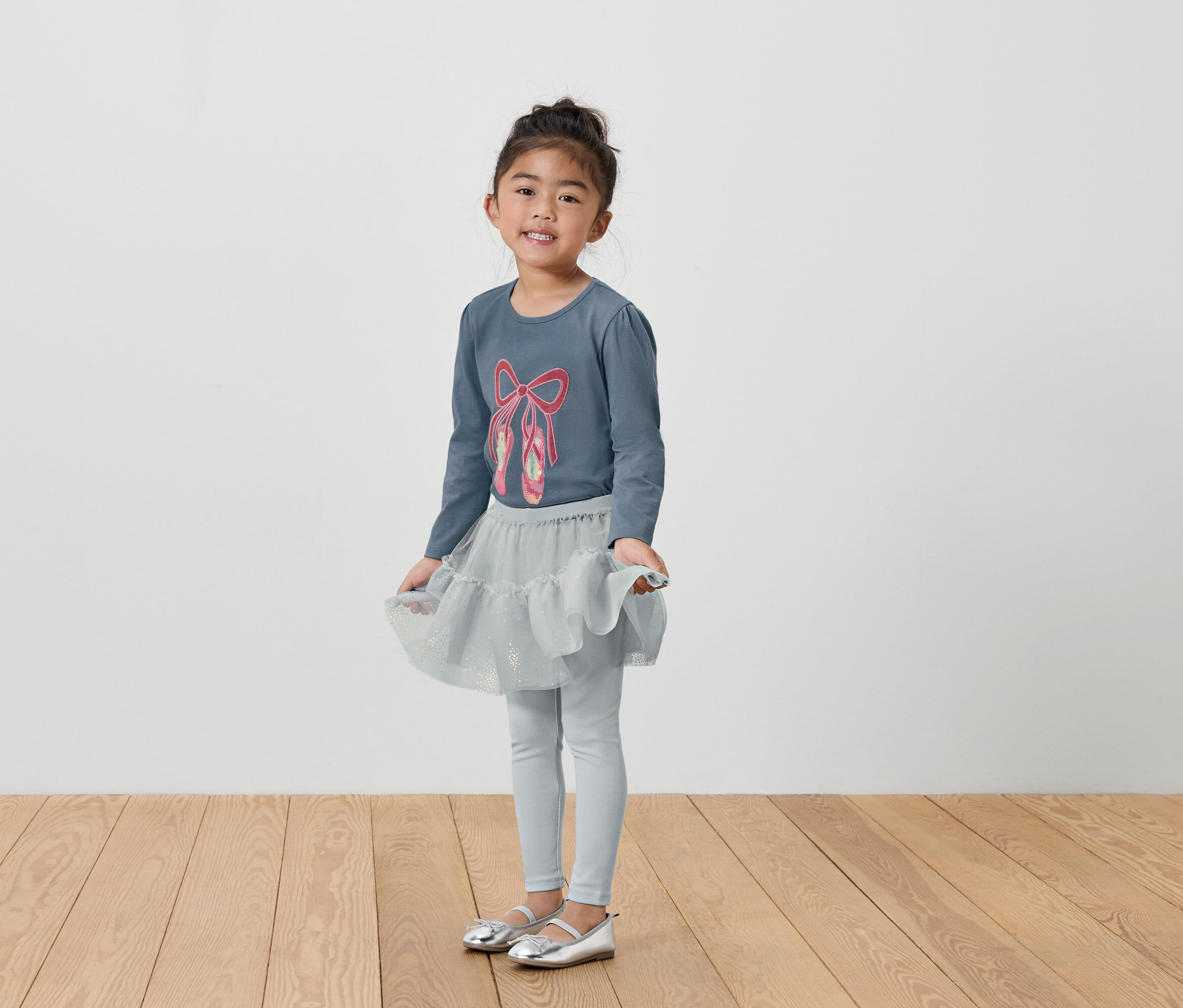 Dziewczynka w szarym stroju baletowym: koszulka, spódnica i legginsy.