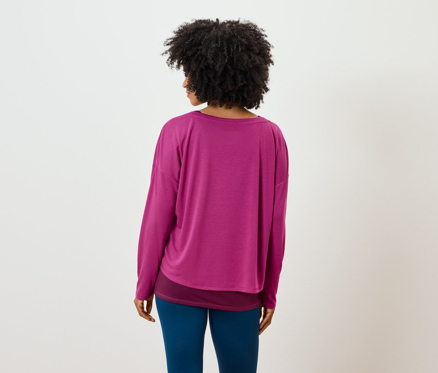 Widok z tyłu na kobietę z fryzurą afro, ubraną w różową koszulkę z długim rękawem i niebieskie legginsy.