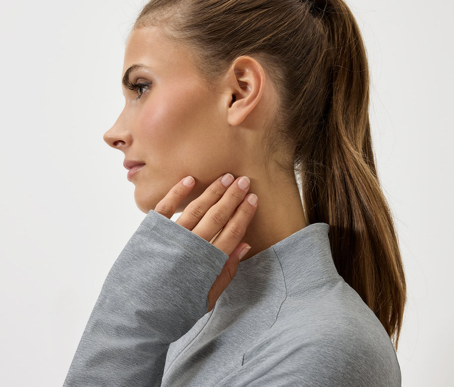 Profil kobiety z brązowymi włosami związanymi w kucyk, dotykającej szyi ręką w szarym swetrze.