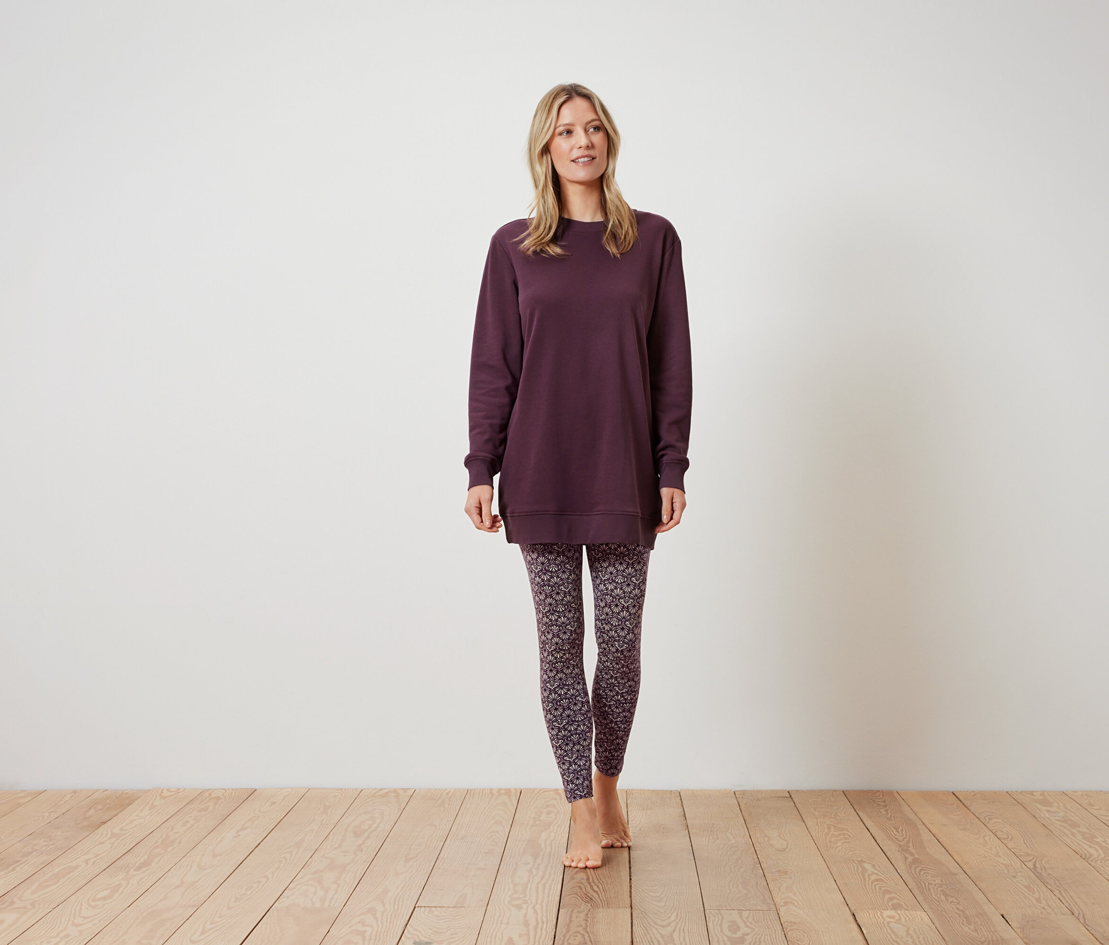 Kobieta stoi w bordowej bluzie i wzorzystych legginsach.