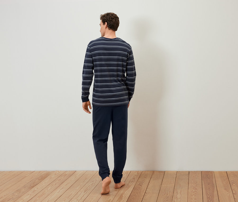Mężczyzna w piżamie w paski idzie boso po drewnianej podłodze.