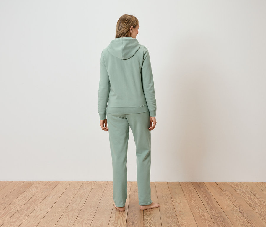 Widok z tyłu kobiety z długimi blond włosami, ubranej w jasnozieloną bluzę z kapturem i pasujące spodnie.