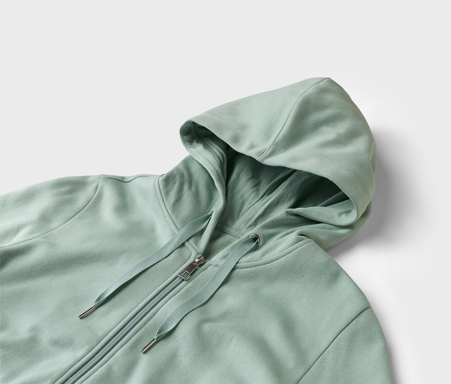 Zbliżenie jasnozielonej bluzy z kapturem i zamkiem błyskawicznym na białym tle.