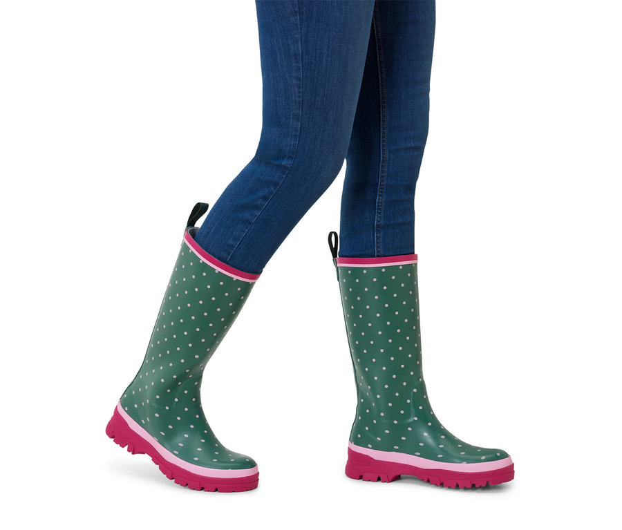 Osoba w niebieskich dżinsach i zielonych kaloszach z różową podeszwą i białymi kropkami.