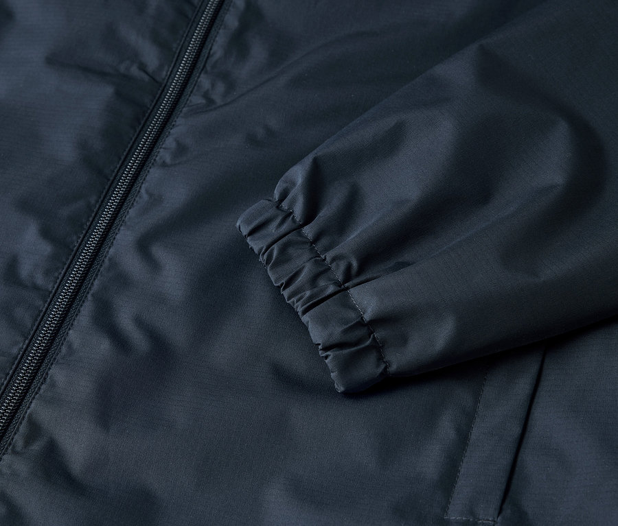 Szczegółowy widok granatowej kurtki z zamkiem błyskawicznym i elastycznymi mankietami.