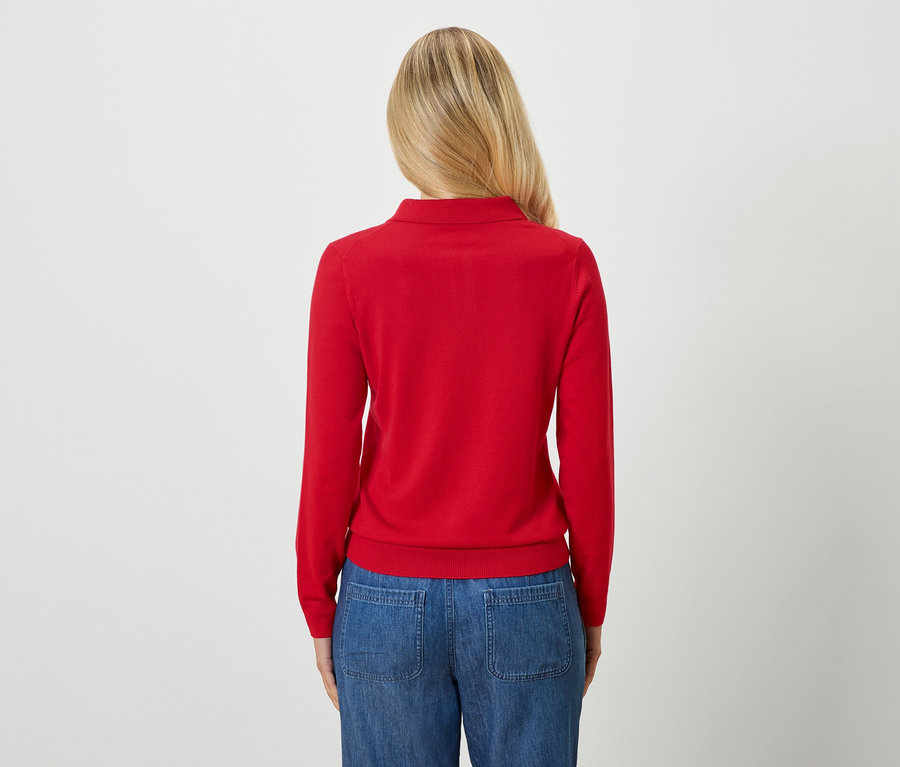 Widok z tyłu kobiety o blond włosach, ubranej w czerwony sweter i niebieskie dżinsy.