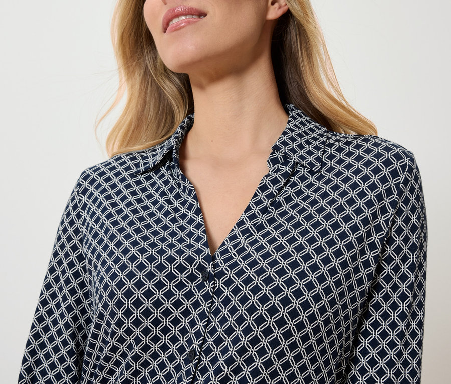 Górna część ciała kobiety w granatowej bluzce w biały geometryczny wzór.