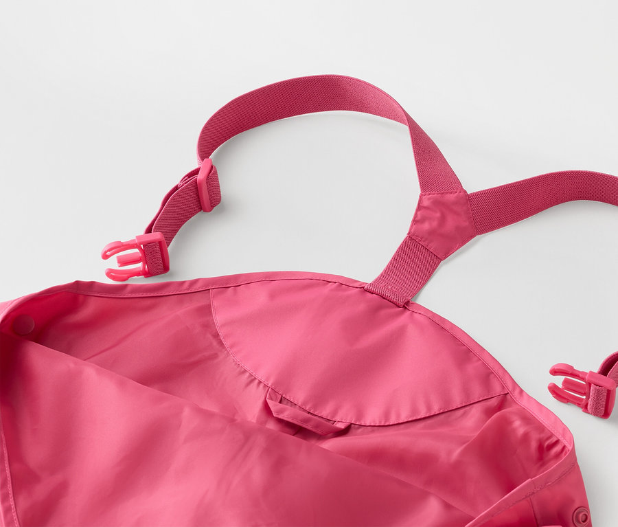 Zbliżenie różowych spodni przeciwdeszczowych dla dzieci z regulowanymi szelkami i klamrami na białym tle.