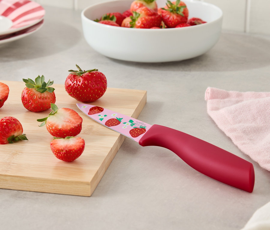 Truskawki i nóż we wzór truskawek na desce do krojenia.