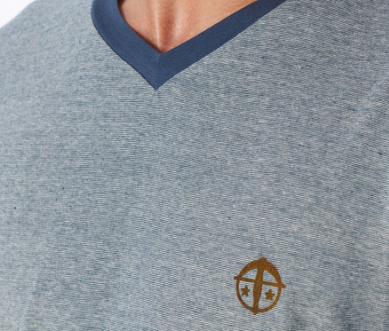 Zbliżenie jasnoniebieskiego t-shirtu z dekoltem w serek, z cienkimi poziomymi paskami i ciemnoniebieskim wykończeniem, z haftowanym złoto-brązowym logo na lewej piersi.