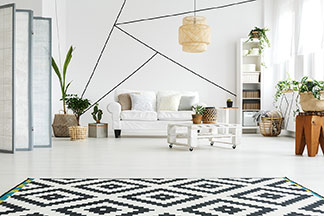 Komplet dwóch stolików: czarna dwuosobowa sofa stoi w salonie pod ścianą w kolorze żółtym. Przed sofą znajdują się dwa okrągłe stoliki o różnej wielkości.