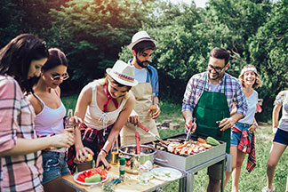 Także warzywa można grillować: Grupka młodych ludzi stoi przy grillu i przygotowuje warzywa na małym stoliku.