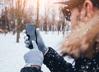 Dodatkowe funkcje rękawiczek dla panów – mężczyzna na tle zimowego krajobrazu obsługuje smartfon w rękawiczkach