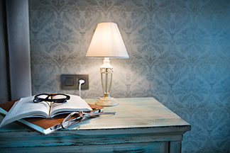 Elegancki design Twojej lampy: lampa stołowa z białym abażurem stoi na stole w stylu vintage, na którym leży mapa, otwarta książka i okulary.