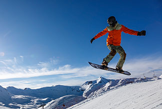 Kurtki sportowe na zimę: snowboardzista podczas skoku na tle ośnieżonych gór.